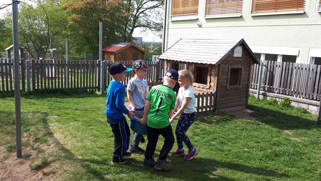 Kinder tragen im Team eine Wanne über die Wiese